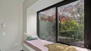 A bedroom with a large window, a bed with a fluffy rug, and a view of trees and a fence. - Brow Peak View - Arrowtown Holiday Home (Arrowtown)