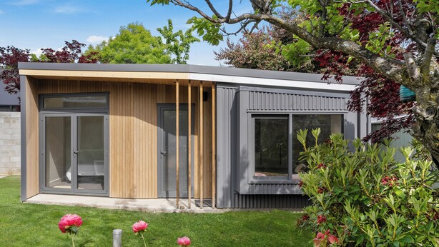 A modern house with a large sliding glass door, a wooden panel wall, and a grey exterior. - Brow Peak View - Arrowtown Holiday Home (Arrowtown)
