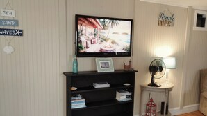 Un salon comprenant un téléviseur, une bibliothèque, une petite table avec un ventilateur et un mur décoré de panneaux.