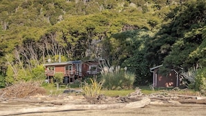 Une cabane dotée d’une terrasse, entourée d’une forêt dense et accessible par un chemin de gravier.