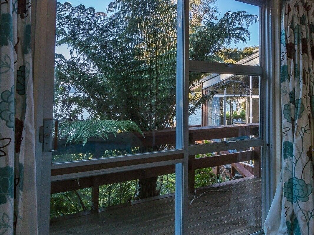 Une terrasse en bois avec des garde-corps en verre donnant sur un jardin luxuriant.