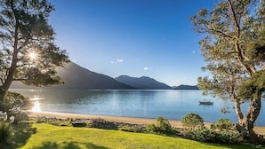 Une vue paisible sur un lac, avec un bateau, des zones herbeuses et des montagnes en arrière-plan.