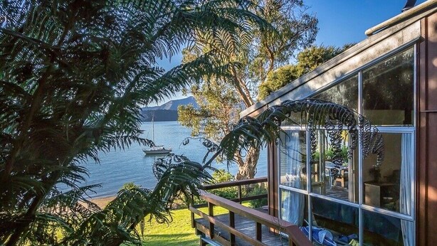 Une maison moderne dotée d’un balcon en verre donnant sur un lac et des montagnes.