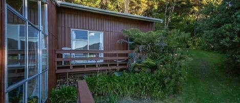A wooden cabin with a deck, surrounded by lush greenery and trees.