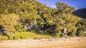 Une maison de plage avec vue sur l’océan et sur une colline boisée.