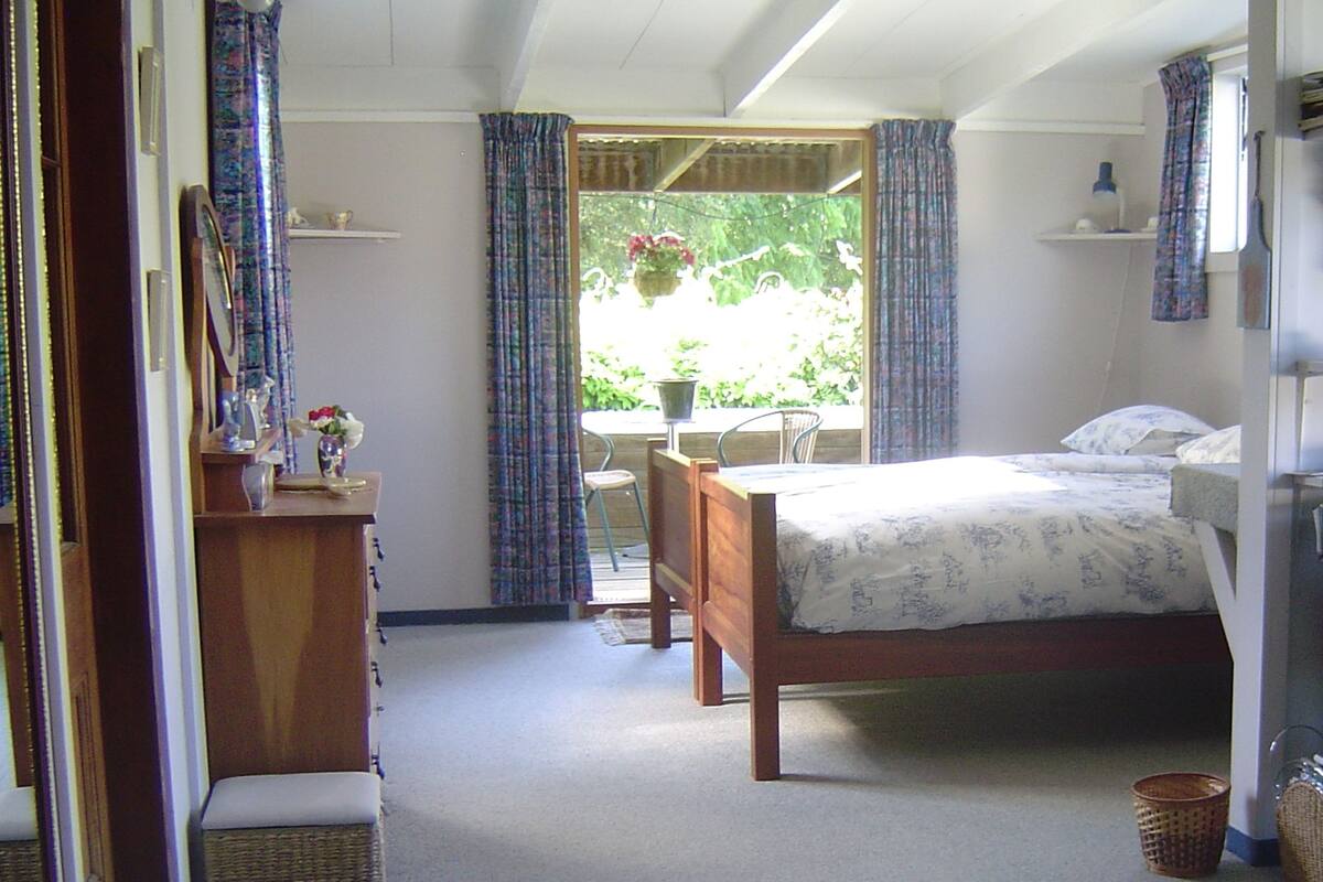 Une chambre à coucher avec un lit, une commode, une chaise et une fenêtre avec des rideaux.