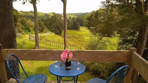 A wooden deck with two blue metal chairs and a table, overlooking a green landscape with hills and a fence. - Mairenui Rural Retreat (Rangiwahia)
