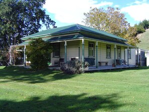 A two-story house with a green roof and white walls, featuring a porch with outdoor seating. - Mairenui Rural Retreat (Rangiwahia)