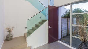A modern interior with a glass staircase, a red door, and a view of a garden. - Ocean Escape - Omaha Holiday Home (Omaha)