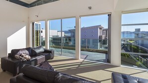 A spacious living room with a large sliding glass door leading to a balcony. There are two leather sofas and a coffee table. - Ocean Escape - Omaha Holiday Home (Omaha)