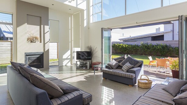 A modern living room with a fireplace, comfortable seating, and a large glass door leading to an outdoor patio. - Ocean Escape - Omaha Holiday Home (Omaha)