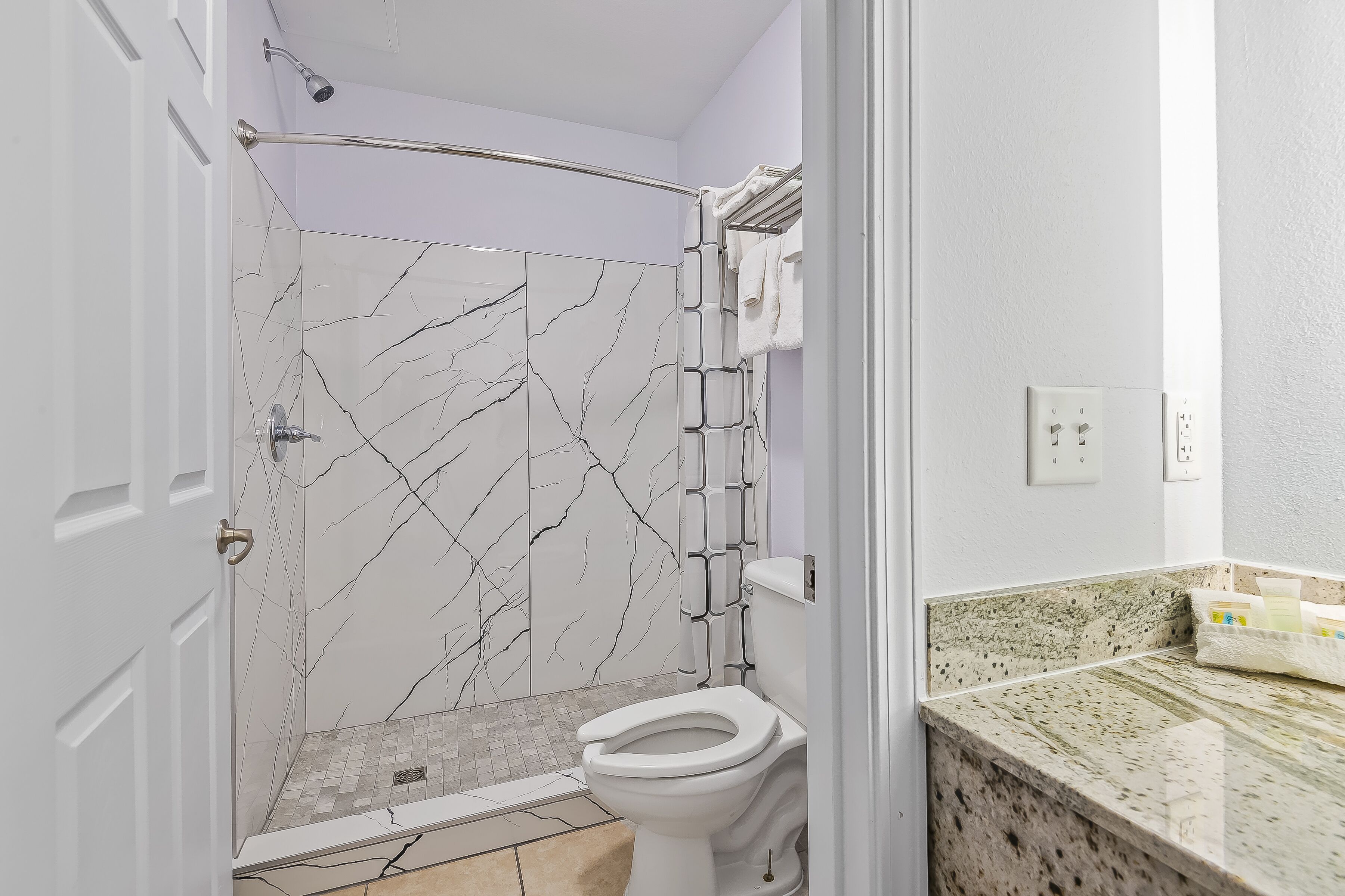 Baño con ducha, inodoro y encimera de granito.