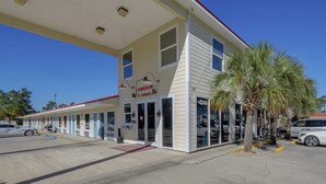 A motel with a single-story structure, a covered parking area, and a palm tree in front.