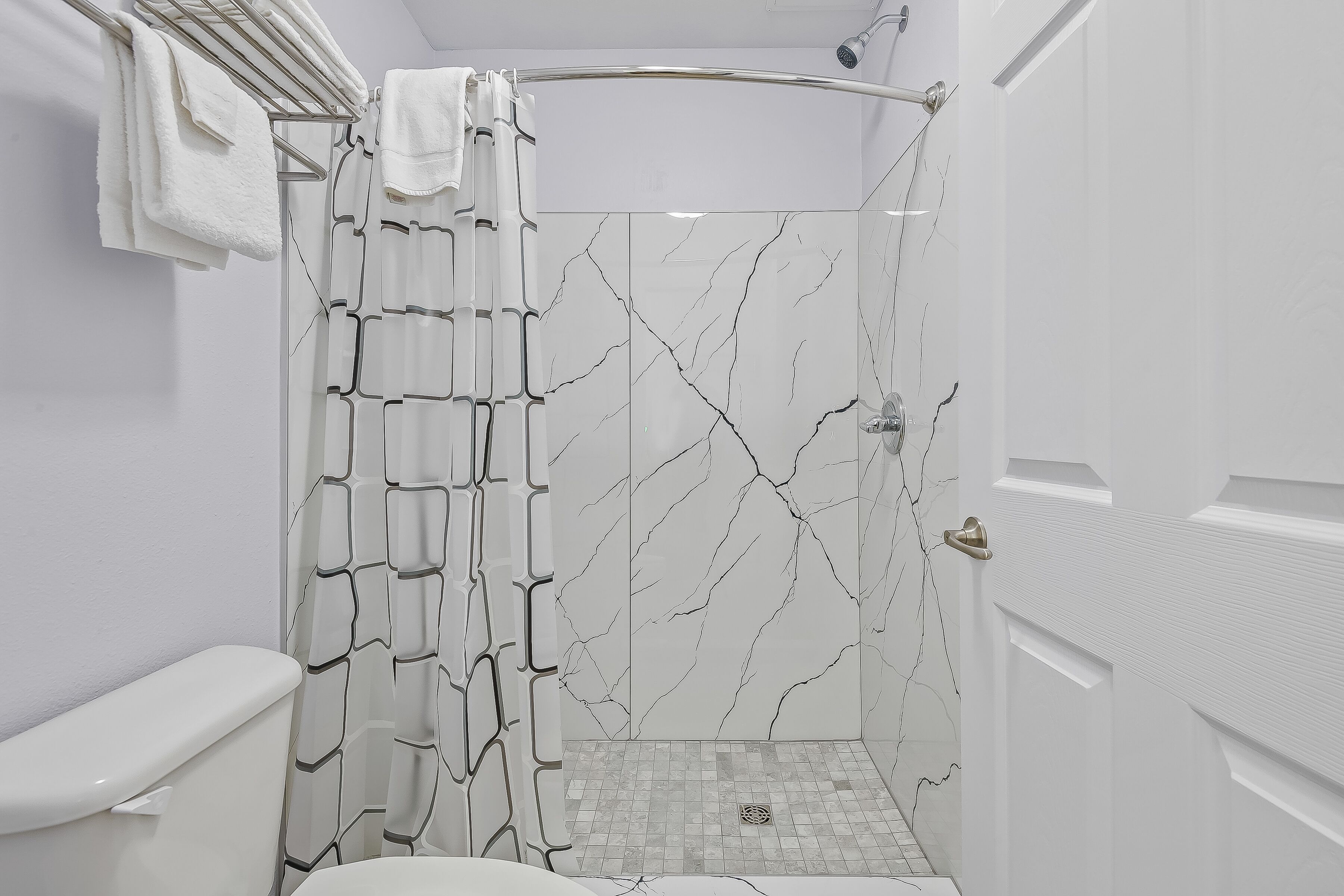 Une salle de bain moderne avec une douche, des carreaux blancs et un mur décoré d’un motif imitant le marbre.