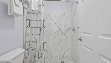 Une salle de bain moderne avec une douche, des carreaux blancs et un mur décoré d’un motif imitant le marbre.