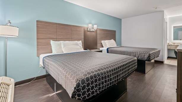 A hotel room with two beds, a nightstand, a lamp, and a bathroom visible through an open door.