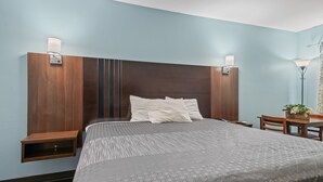 A hotel room with a large bed, two bedside tables, a desk with a chair, and a lamp.