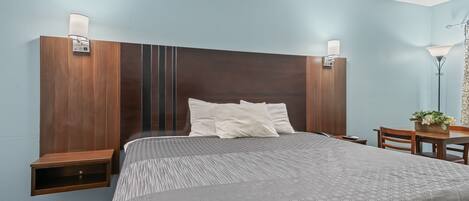 A hotel room with a large bed, two bedside tables, a desk with a chair, and a lamp.
