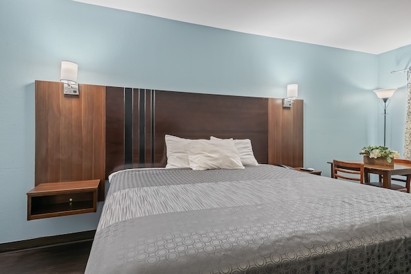 A hotel room with a large bed, two bedside tables, a desk with a chair, and a lamp.