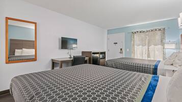 Habitación de hotel con dos camas, un escritorio, un televisor y zona de ducha.