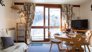 A cozy room with a bed, a dining table with chairs, a TV, and a window with curtains. - Vostok Zodiaque by Interhome (Le Corbier)