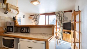 A compact kitchen with a coffee maker, microwave, and refrigerator. There is a wooden shelf with a television and a wooden cabinet in the background. - Vostok Zodiaque by Interhome (Le Corbier)