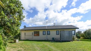 A single-story house with a tiled roof, a satellite dish, and a fenced yard. - Arawai - Waimarama Holiday Home (Waimarama)
