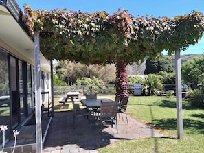 Une terrasse couverte avec une table et des chaises, une pergola ornée de plantes grimpantes et une vue sur le jardin et les collines environnantes.