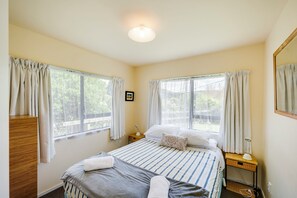Una habitación de hotel con cama, mesitas de noche, un espejo y ventanas con cortinas.
