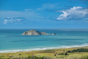 Un paisaje costero con una isla rocosa destacada en el mar, una playa en primer plano y un cielo despejado.