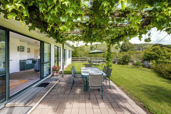 A modern house with a patio, a dining table with chairs, and a view of the surrounding landscape.