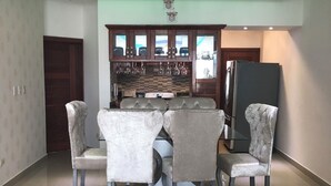 Un coin repas avec une table ronde et quatre chaises, une cuisine équipée de placards et d’un réfrigérateur, et une porte donnant sur une autre pièce.