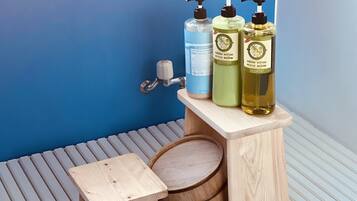 A wooden vanity with three bottles of toiletries: a blue liquid soap, a green conditioner, and a yellow shampoo.