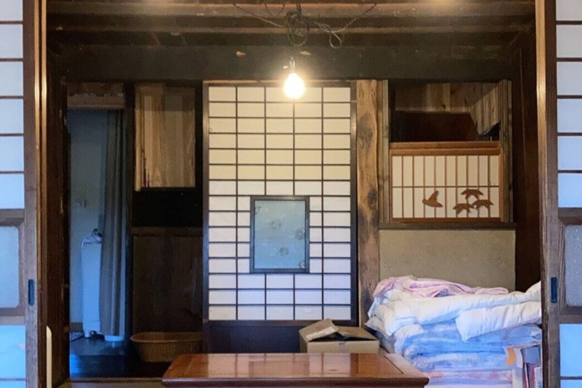 A traditional Japanese room with tatami flooring, a low wooden table, a futon bed, and a shoji screen with a framed picture.