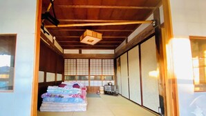 Una habitación japonesa tradicional con suelo de tatami, futón, puertas correderas y una pequeña cocina con hervidor.