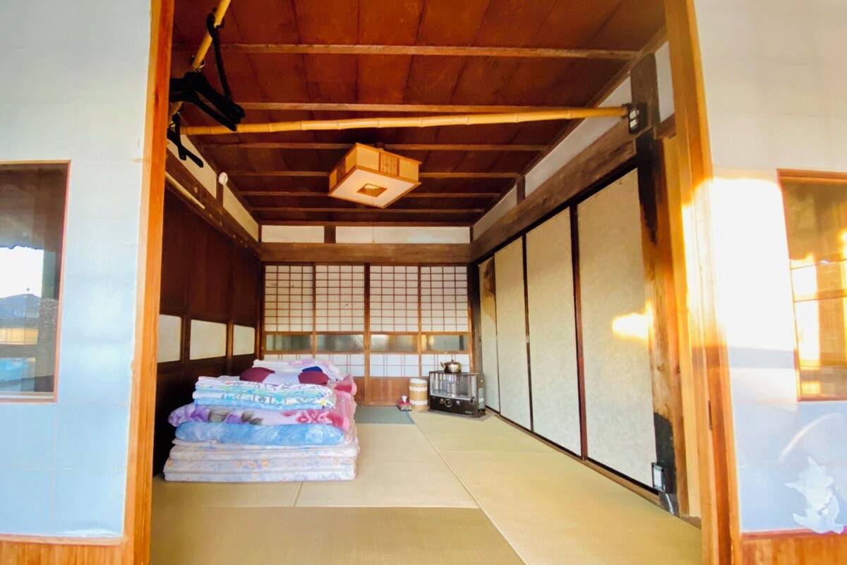 A traditional Japanese room with tatami flooring, a futon bed, sliding doors, and a small kitchen area with a kettle.
