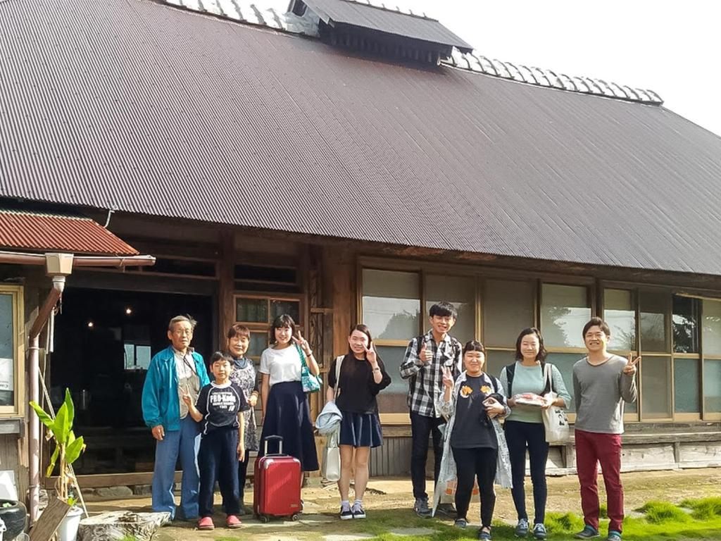 A group of people standing in front of a building with a large window and a metal roof.