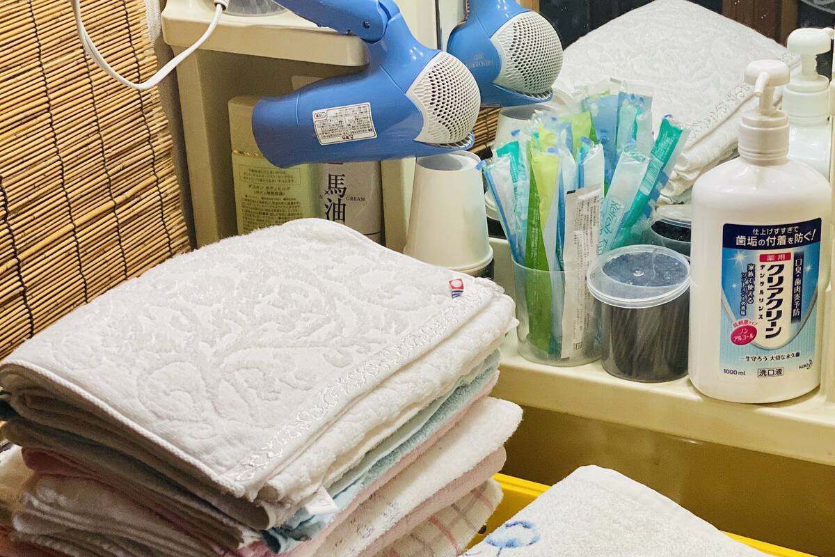 A bathroom with a stack of folded towels, a hairdryer, and toiletries on the counter.