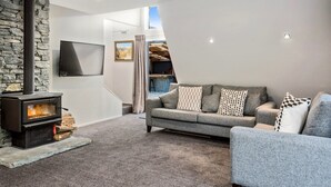 En moderne stue med en stenvæg, pejs, en grå sofa og et fjernsyn monteret på væggen.