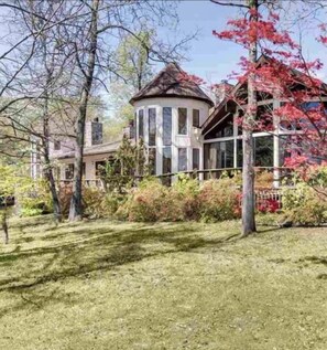 A modern house with a circular tower, surrounded by a well-maintained garden and trees with autumn leaves.
