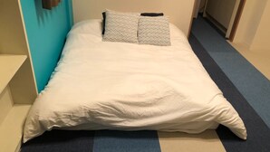 A single bed with white bedding and patterned pillows in a room with a blue and beige carpet. - Oval Tokyo Ikesan 101 (Tokyo)