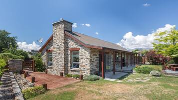 A stone house with a wooden deck, a covered patio, and a garden.