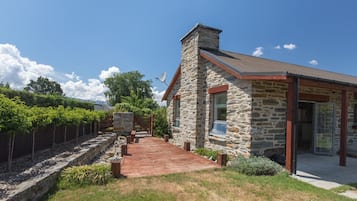 A stone house with a wooden deck, a stone wall, and a garden with young trees.