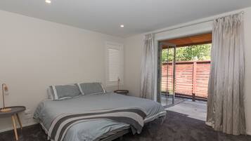A bedroom with a bed, a bedside table, a window with curtains, and a view of the outside.