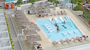 A rooftop pool area with multiple lounge chairs and umbrellas, a swimming pool, and a view of the surrounding cityscape. - Ilikai Luxury Suites (Honolulu)
