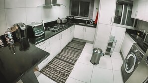 Eine moderne Küche mit weißen Schränken, einer schwarzen Arbeitsplatte, einem eingebauten Herd, einer Mikrowelle und einer Waschmaschine.