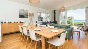 Un comedor moderno con una mesa de madera y sillas blancas, un sofá verde y vistas al océano.