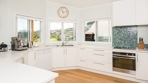 Una cocina moderna con armarios blancos, horno empotrado, cafetera y vistas al exterior a través de amplios ventanales.