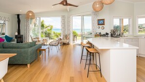Amplia sala de estar con sofá, mesa de comedor y sillas, cocina con una isla grande, y ventanas amplias con vista al mar.