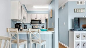 A compact kitchen with white cabinets, a microwave, a coffee maker, and a small island with bar stools.